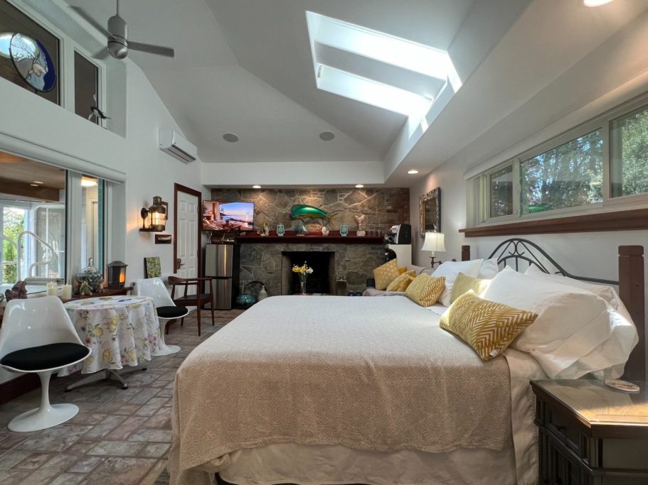 Luxury Guest Suite Panoramic Interior View Wide panoramic view of the luxury guest suite showing the open layout, breakfast dining table, king bed, and stone fireplace at Wind in the