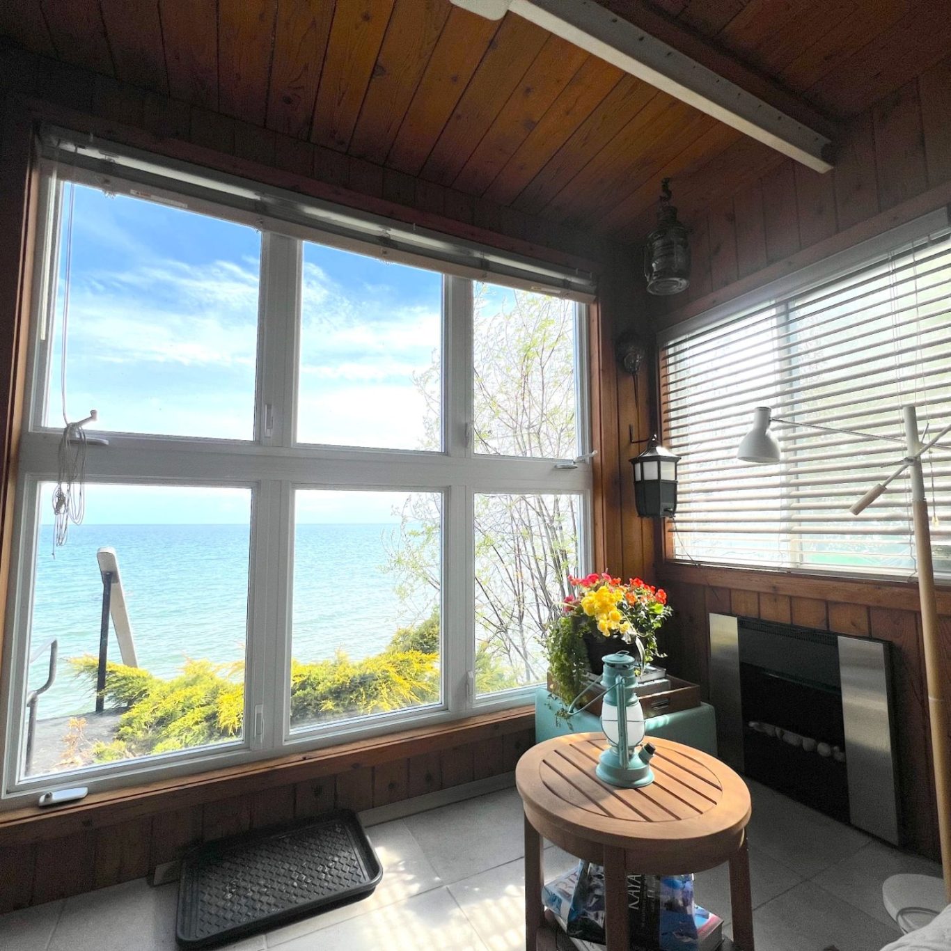 Moles Den Lakeview Room with Stained Cedar Wood A cozy indoor hillside den featuring stained cedar wood paneling, an electric fireplace, and large panoramic windows looking out at Lake ON